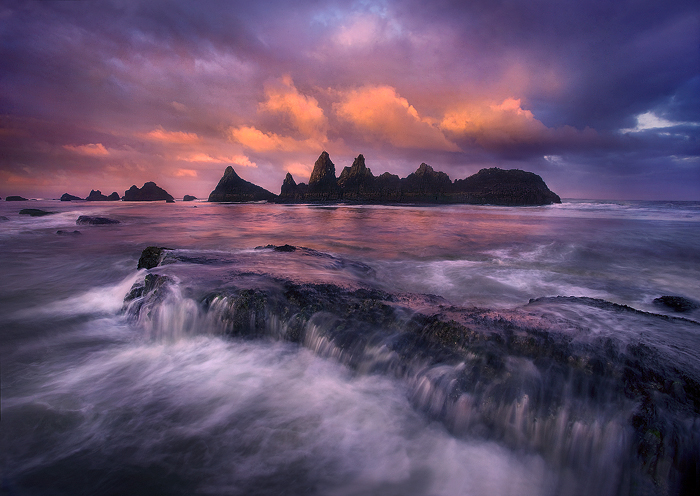 Dramatic light over sea stacks at Seal Rock State Park on the Oregon Coast as a wave crashes over the foreground rock.