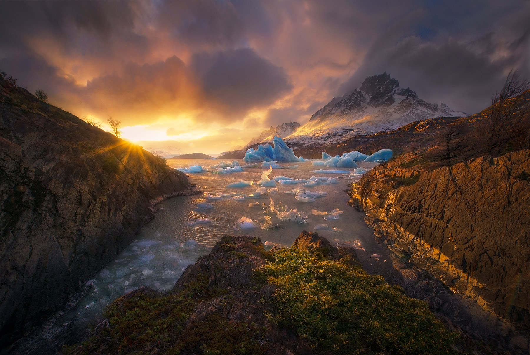 Dramatic light breaks through the clouds above a spectacular sight, icebergs floating atop Lago Grey with Paine Grande Peak in...