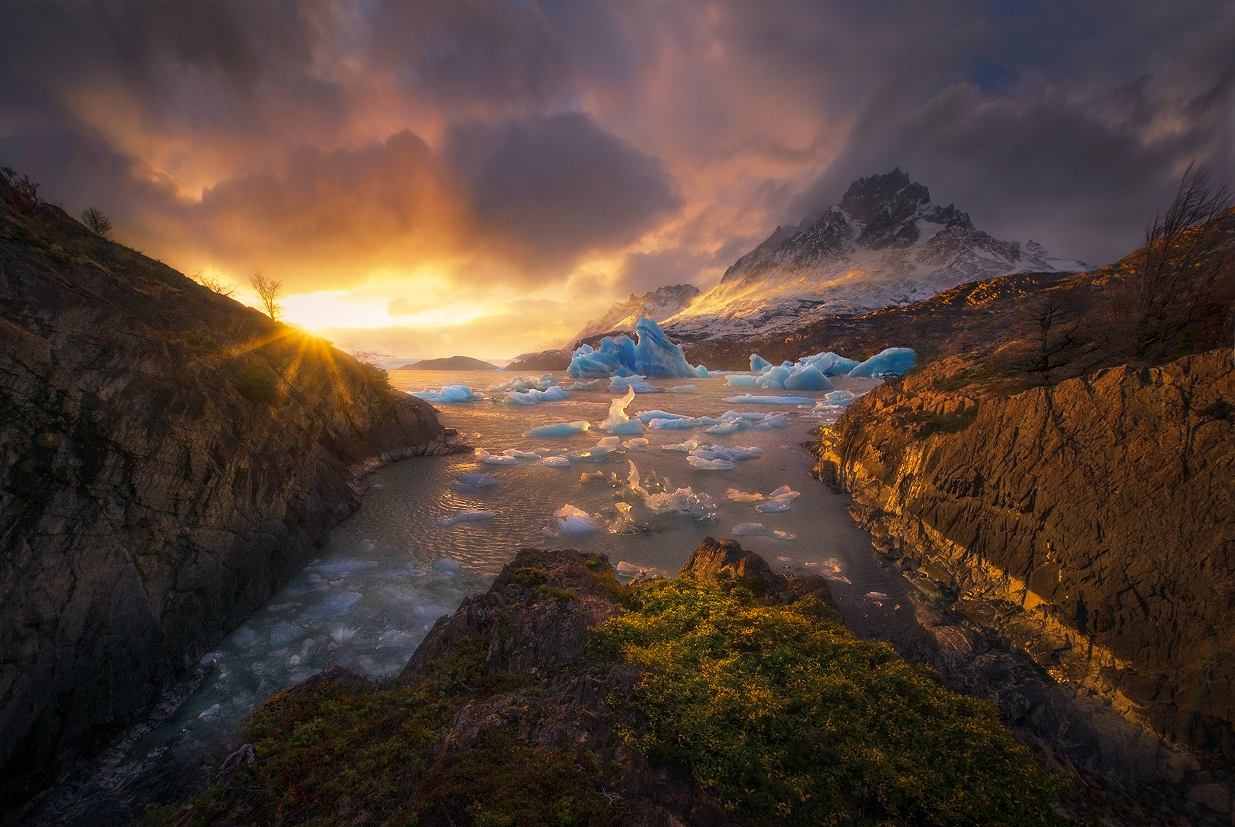 Above the Cold (2013) Dramatic light breaks through the clouds above a spectacular sight, icebergs floating atop Lago Grey with Paine Grande Peak in...
