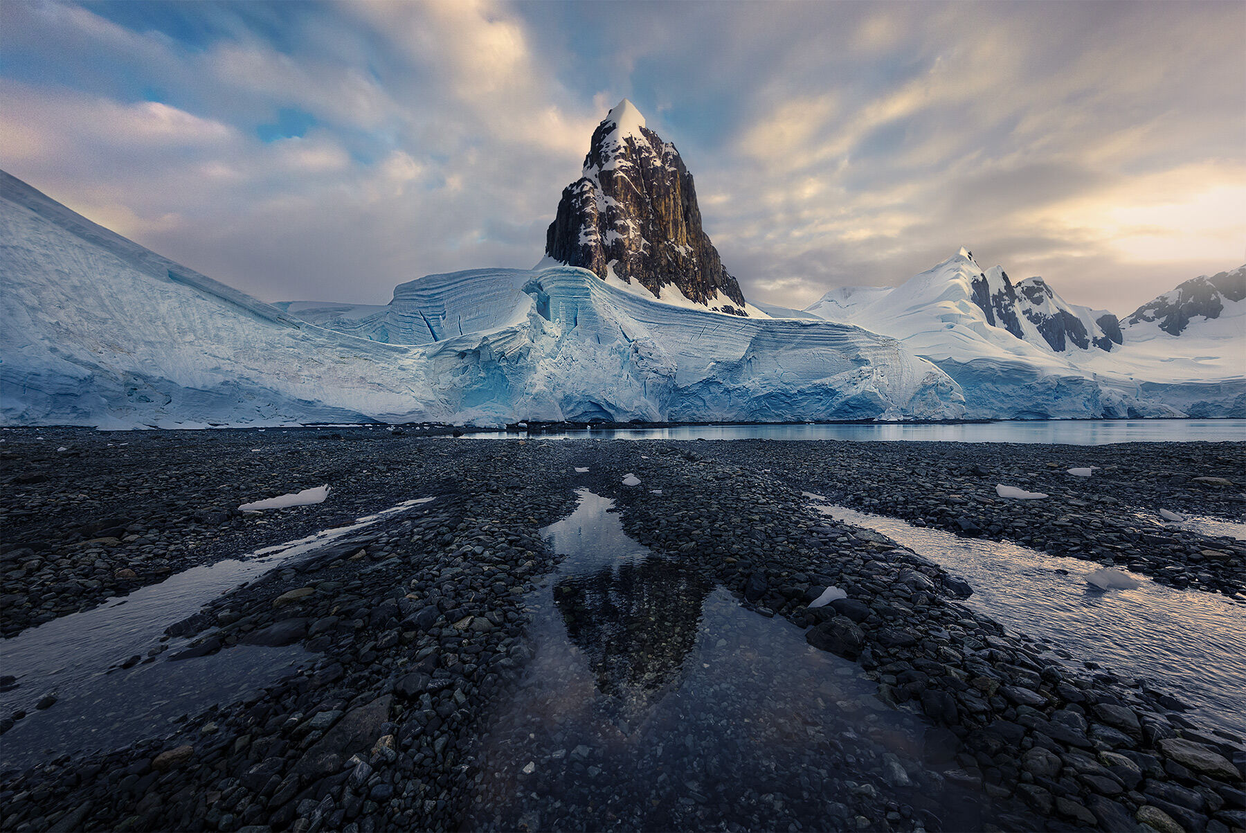 A lone tower reaches from out of the glaciers into sunset light on the Antarctic coast