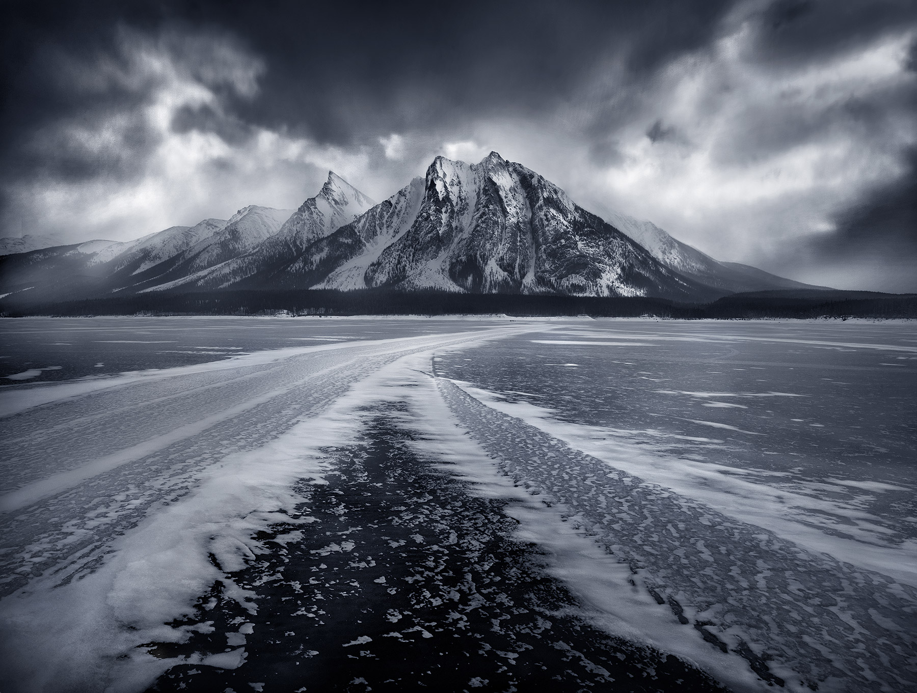 A black and white blue-toned rendition of dramatic skies and ice/snow formations atop the far shore of Spray Lake in the Canadian...