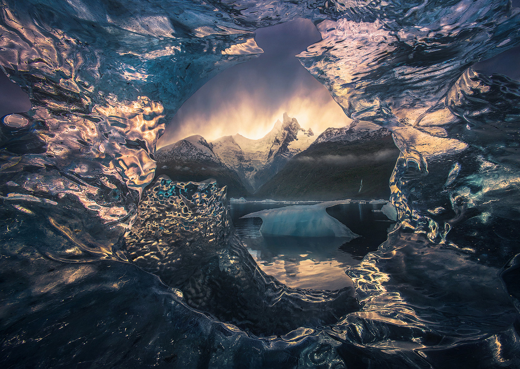 Looking through beached iceberg provides a window through layers of crystal ice framing giant and unexplored peaks beyond in...