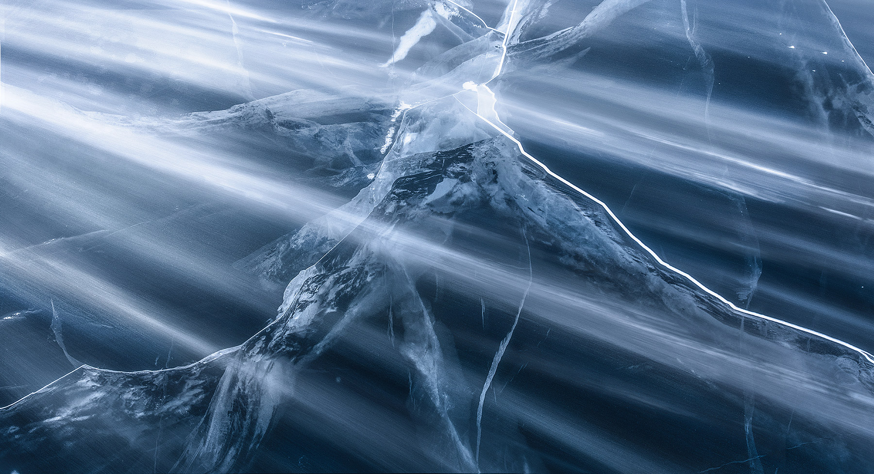 Blowing snow racing across cracks in clear ice below