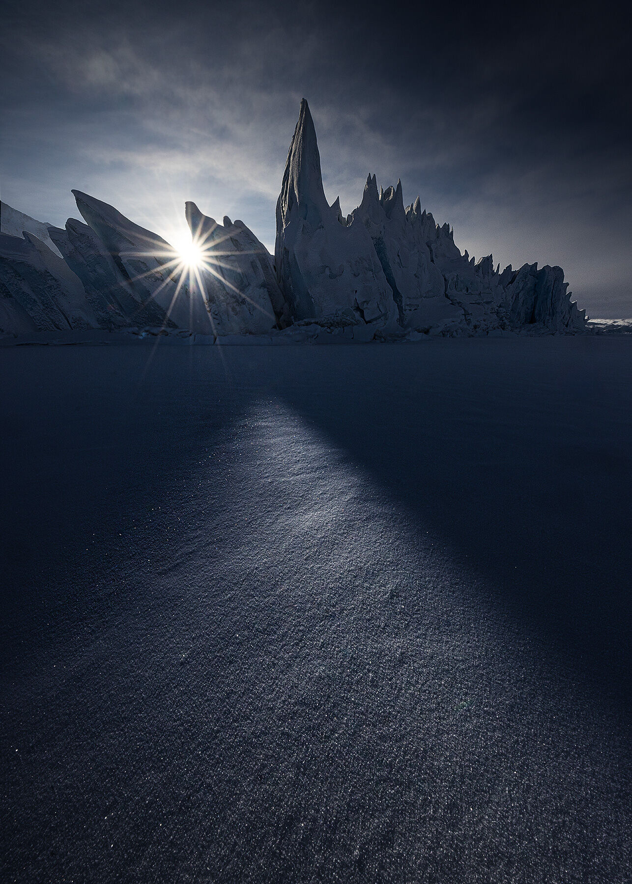 Sunbeams appear on the sparkling snow beneath a jagged glacial face in the Tazlina Valley, Alaska