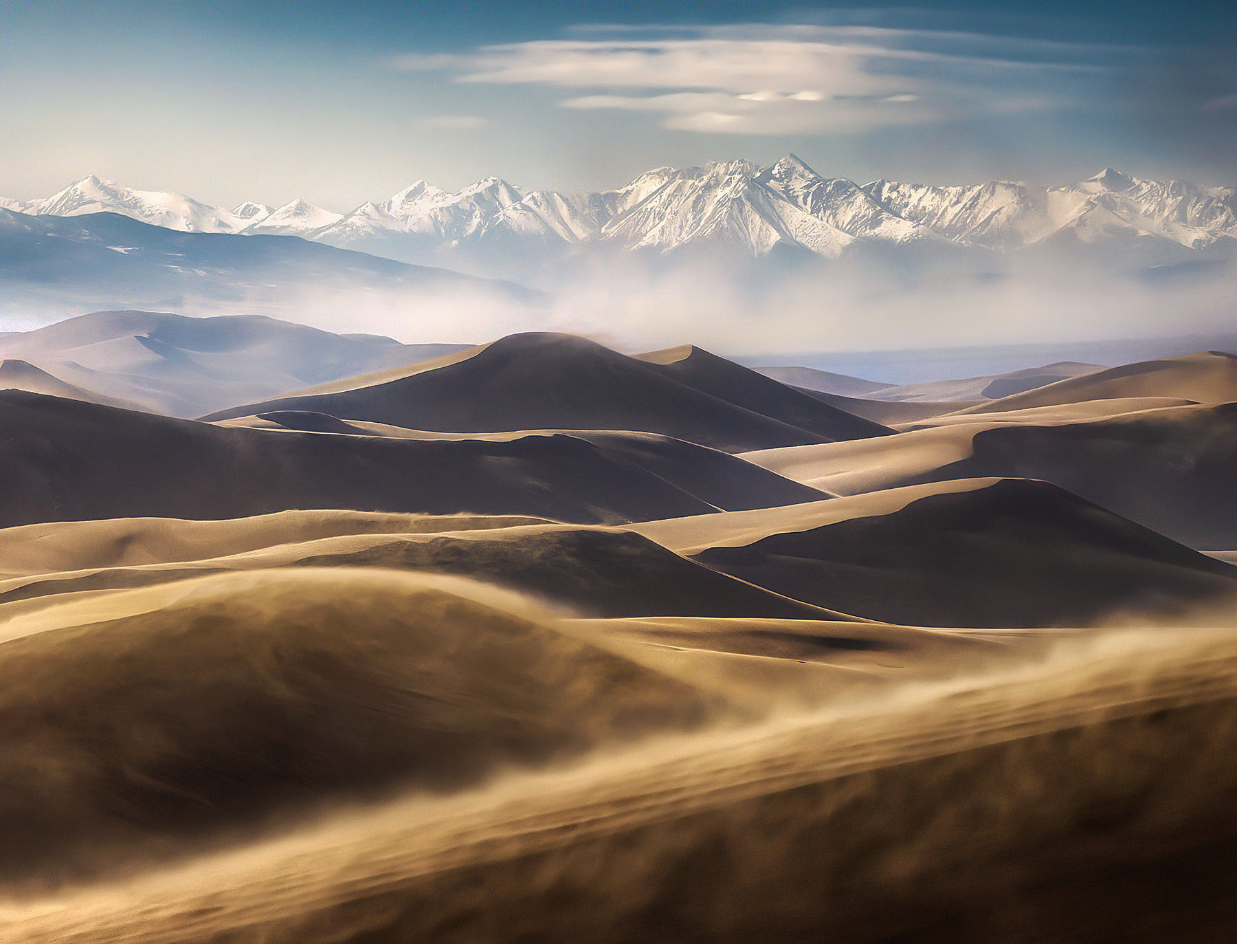 Telephoto layers of dunes and distant mountains amidst blowing sands in Colorado