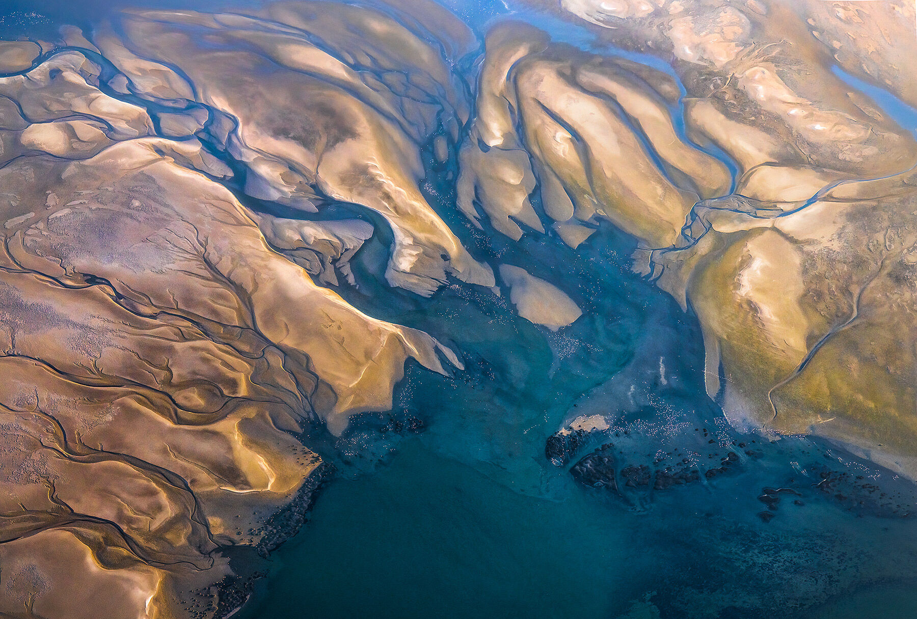 Hundreds of flamingos seen from the air above tidal marshes and desert layers on the west Namibia coastline