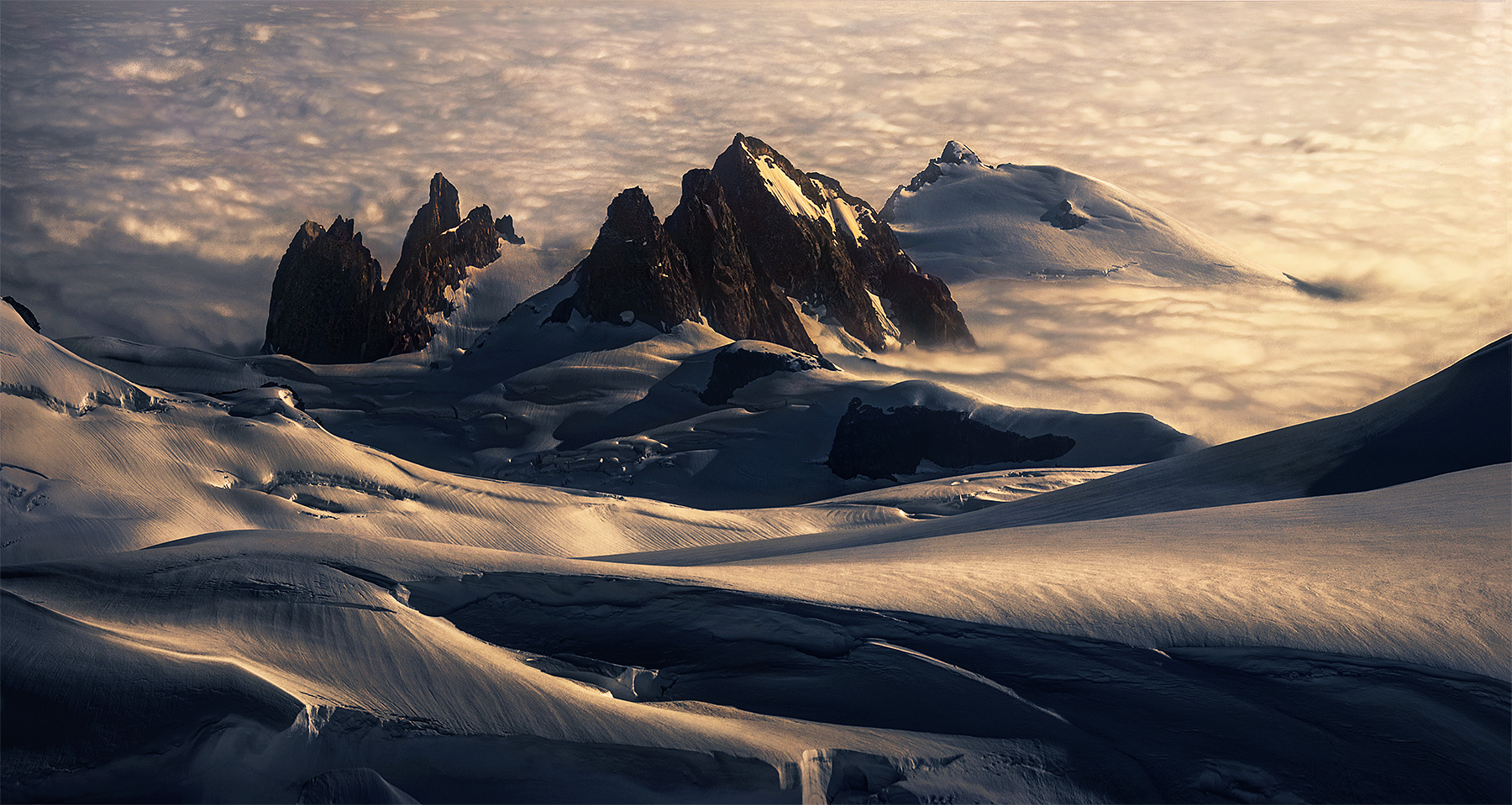 Nameless peaks and enormous glacial snow and ice formations from high in the mountains, above marine layer clouds below.