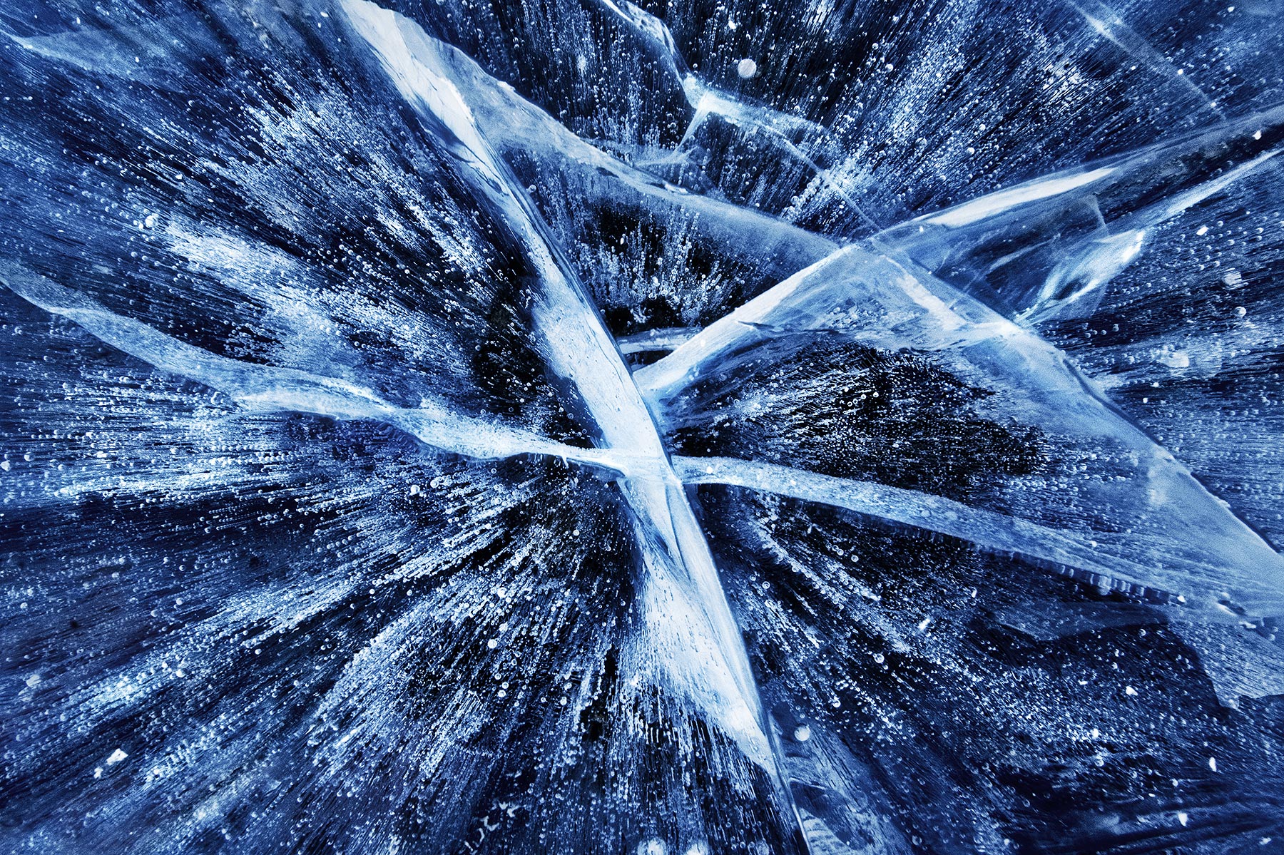 This is a wide-angle abstract of air bubbles and cracks trapped in clear ice on the surface of a lake in the Yukon, Canada, in...