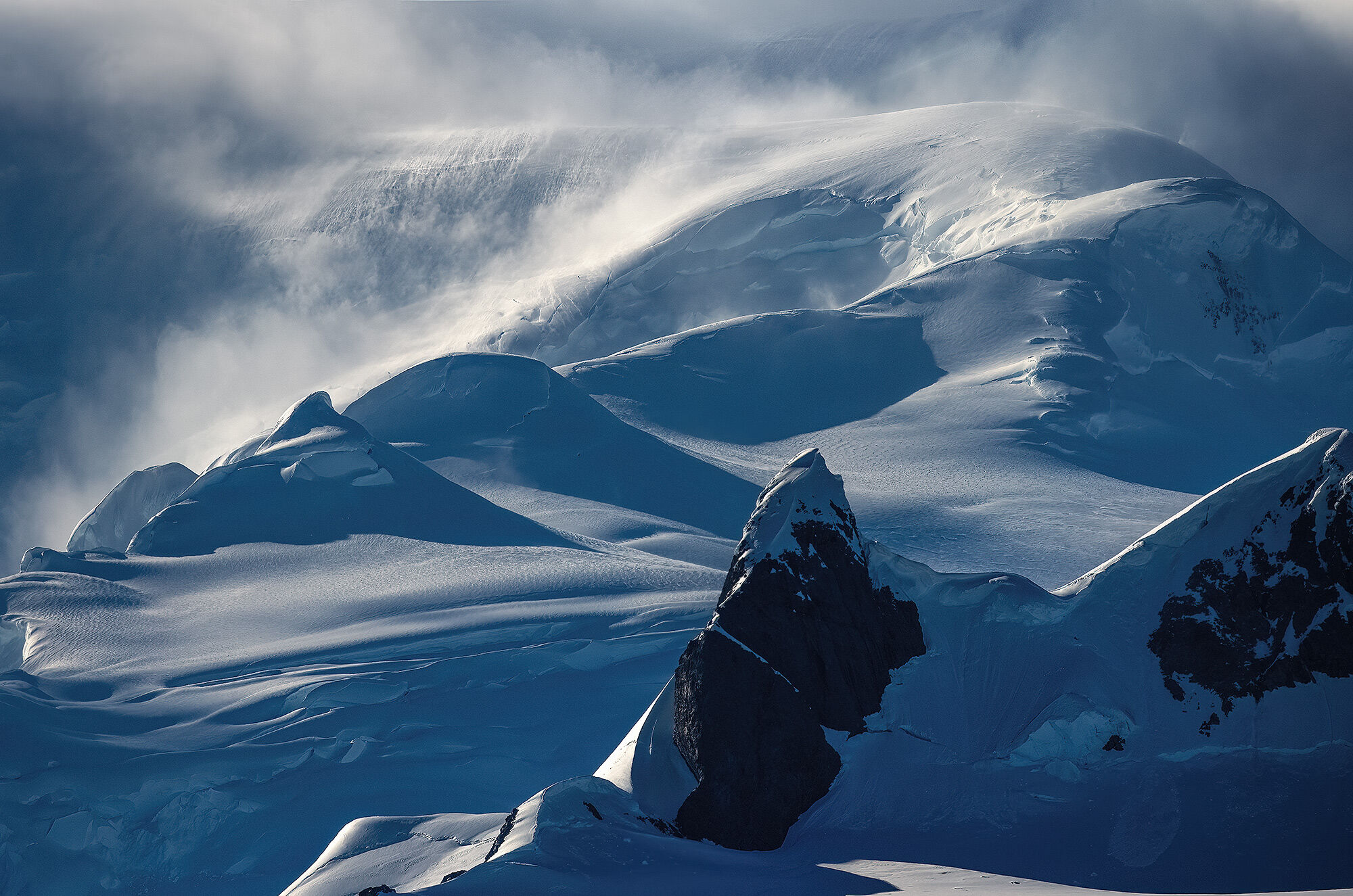 Jagged summits and blowing waves of snow and clouds pouring off the Antarctic continent in the morning light