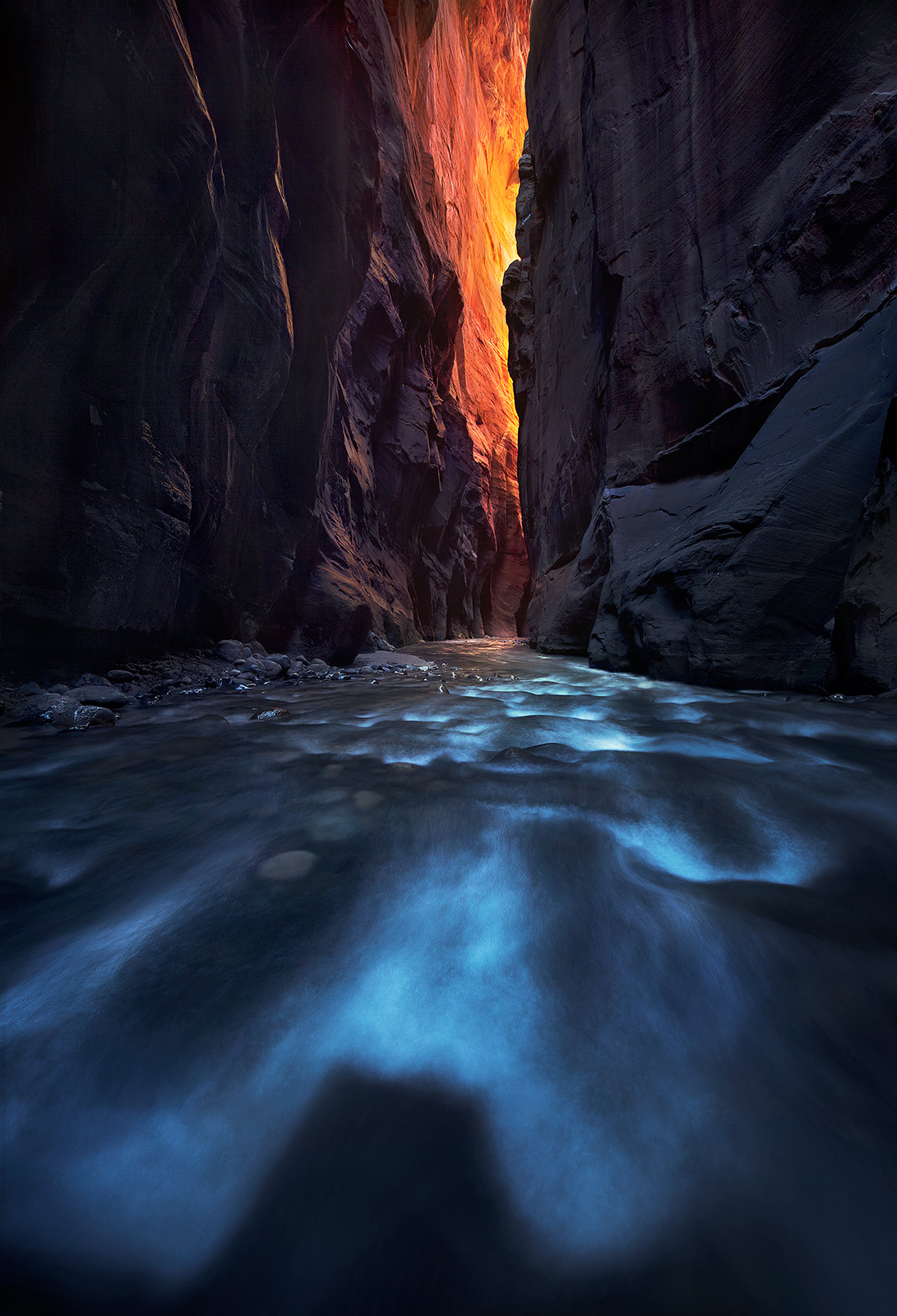 Cool river waters flowing towards the reflected light in the darkest part of Zion's famous Narrows.