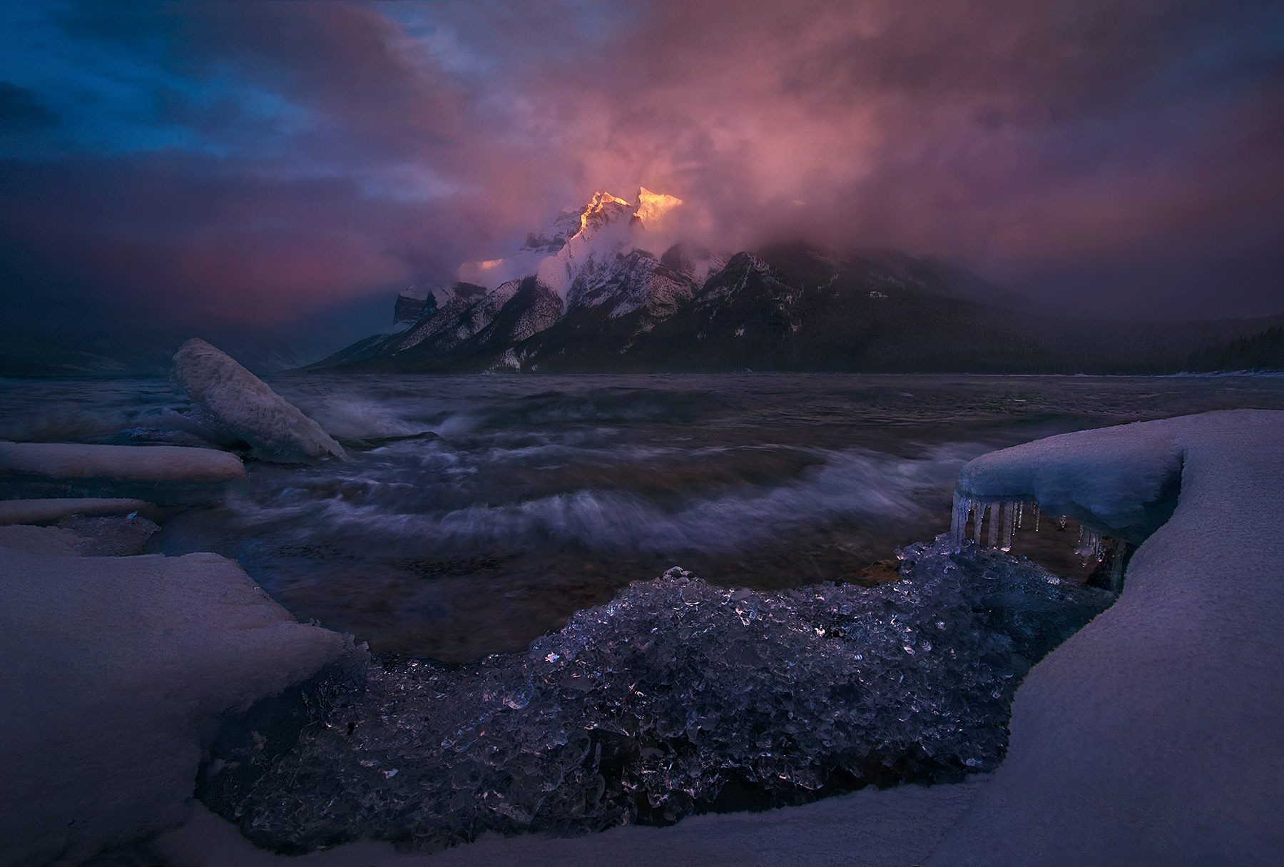 The last light of sunset emerges from the storm above an icy and turbulent lake Minnewanka in the Canadian Rockies.