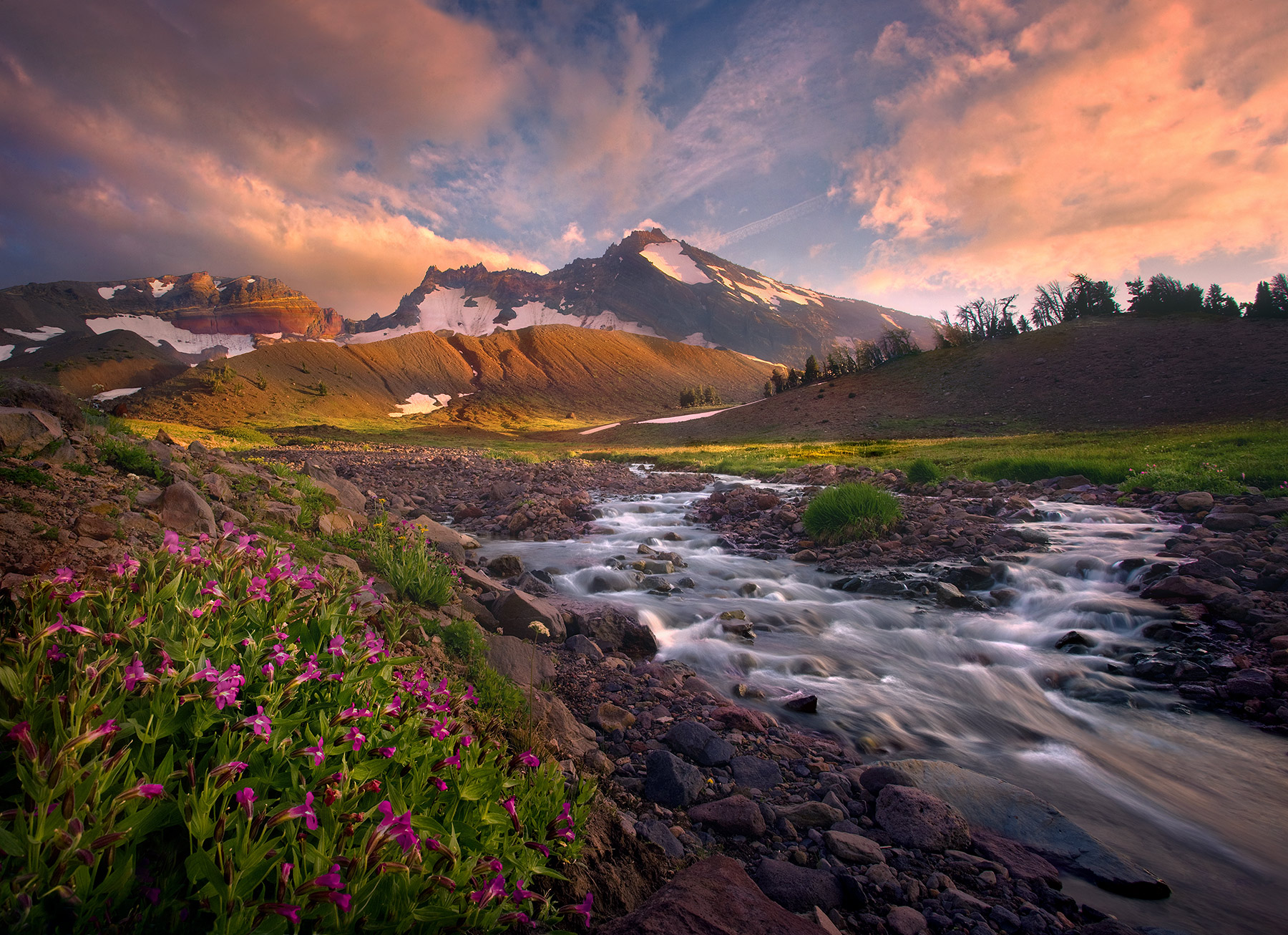 Mountain wildflowers and icy cool glacial stream waters lead the way towards a beautiful sunset over Broken Top peak in Oregon...