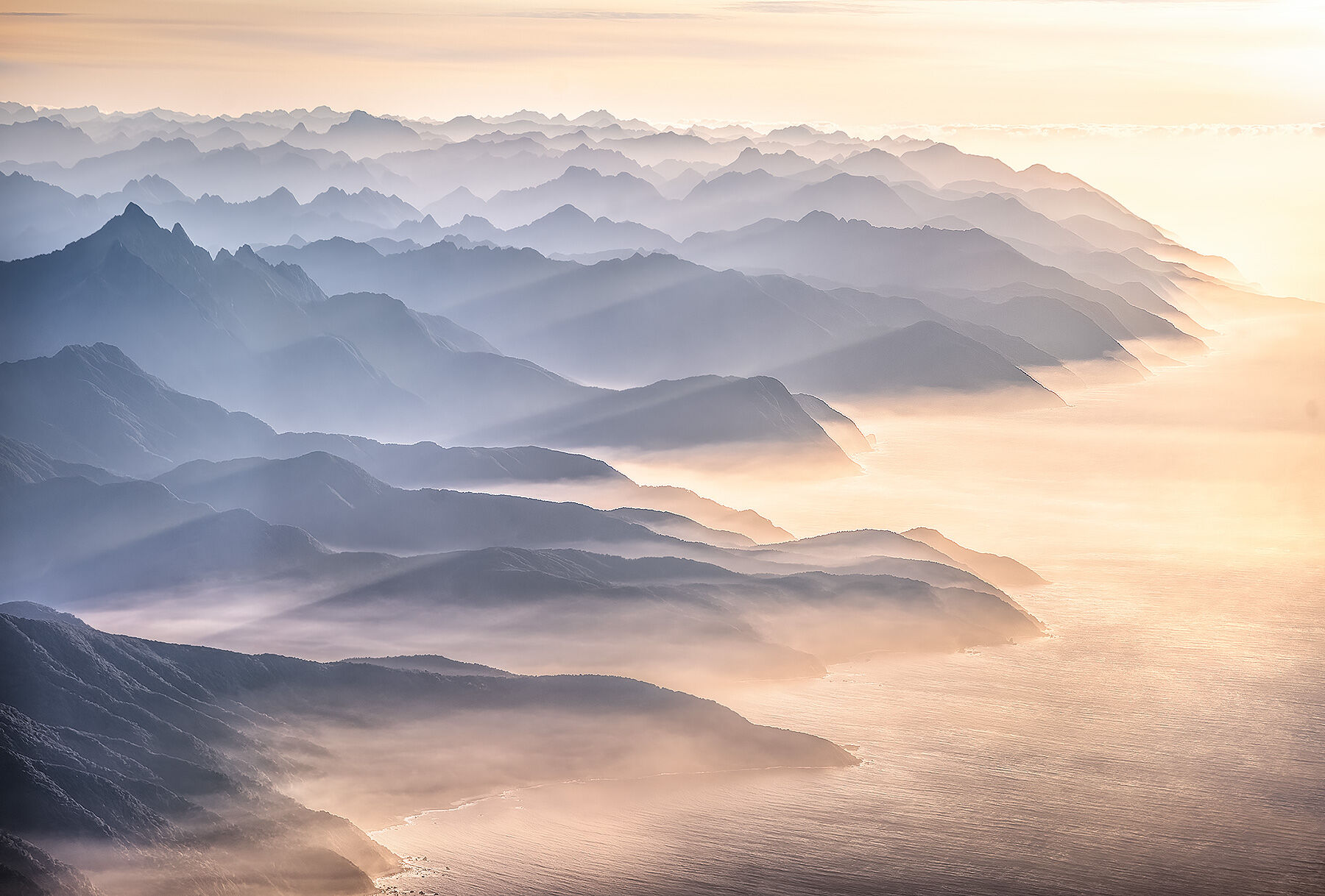 The endless misty layers where Fiordlands meets the Tasman sea at sunset from the air