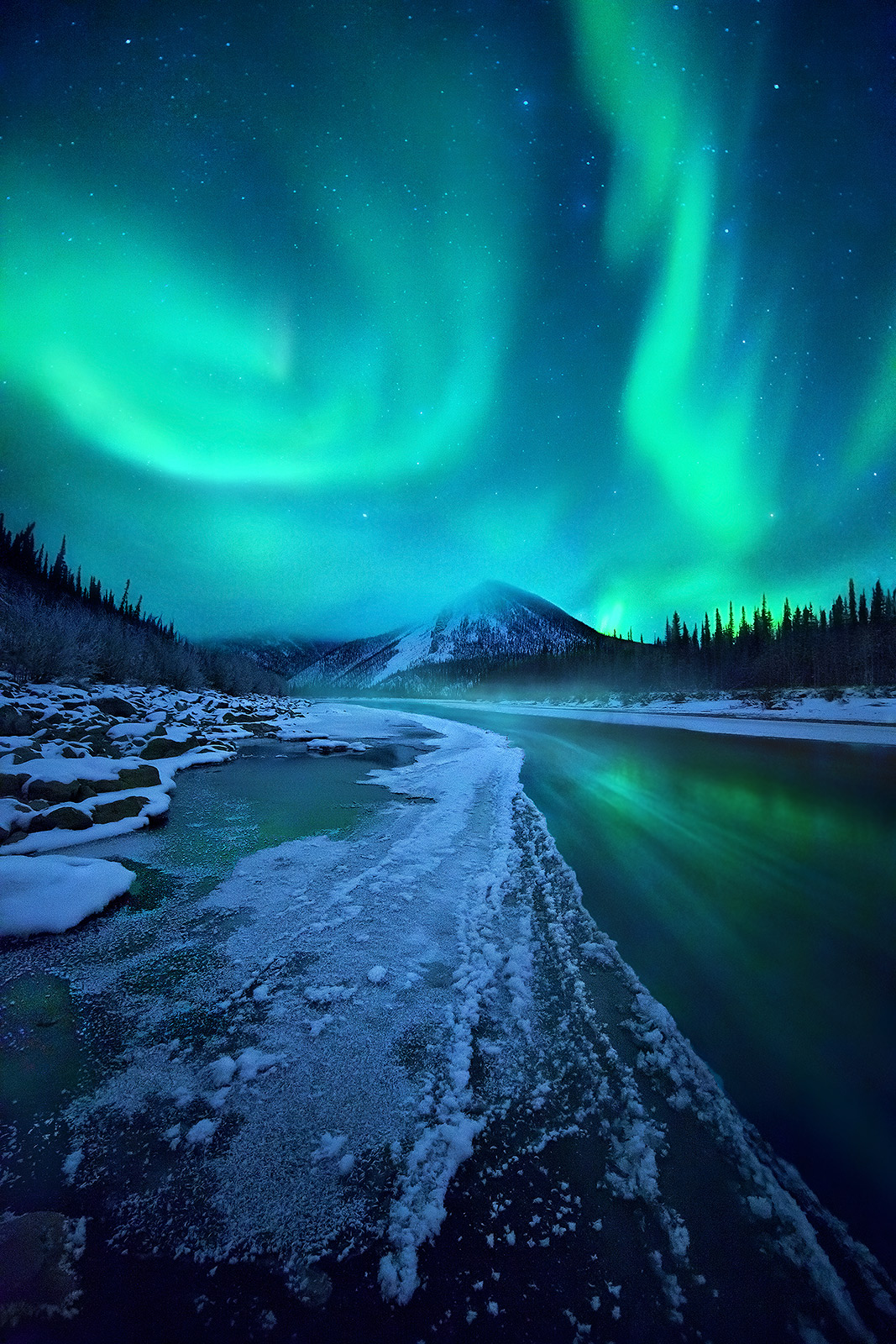 Spectacular colors of the Aurora over the Ogilvie Mountains, Yukon Territory. Streaks in the water from ice floating down river...