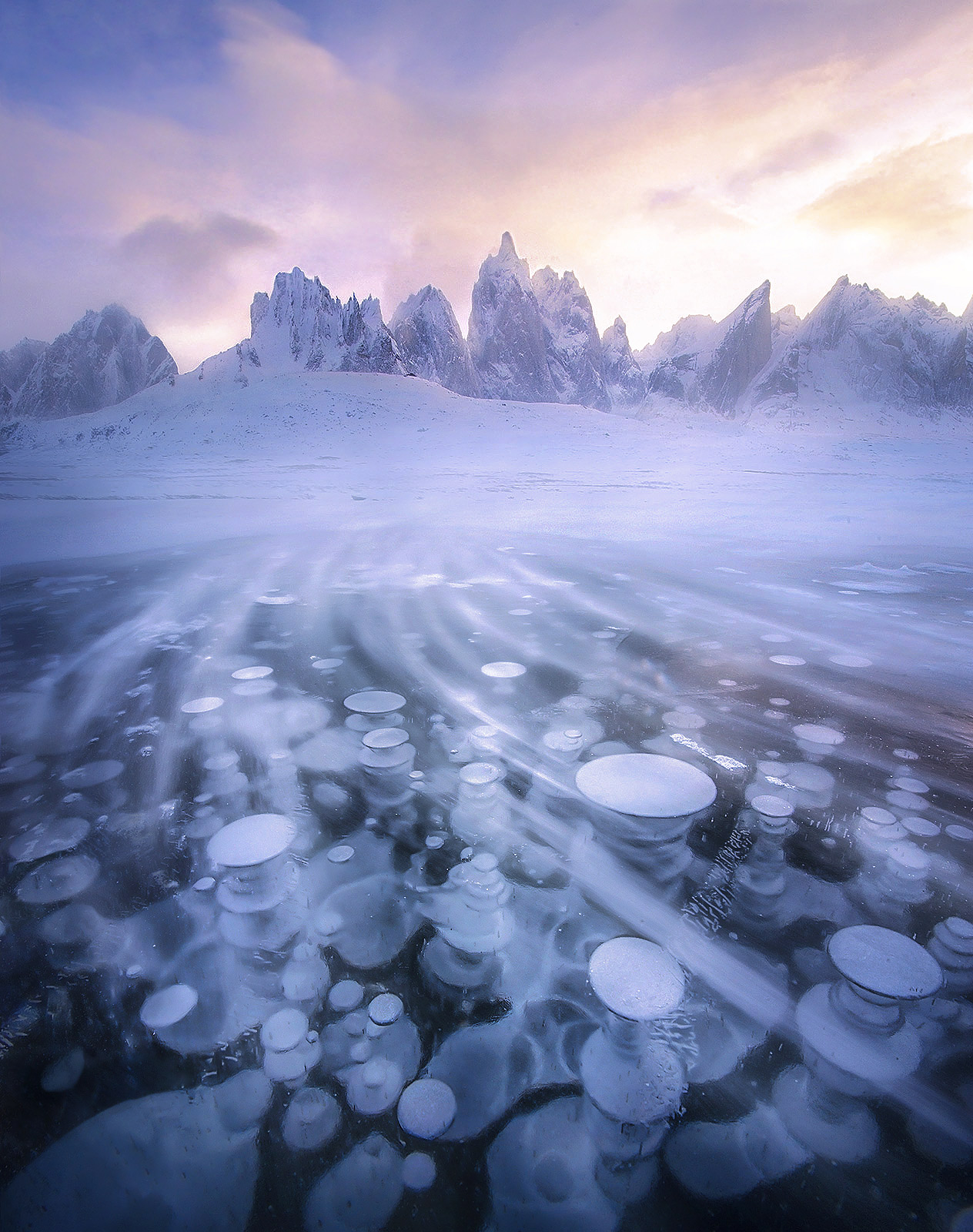 This photograph of ice bubbles and blowing snow on a lake underneath Mount Monolith and other peaks in the Yukon probably has...