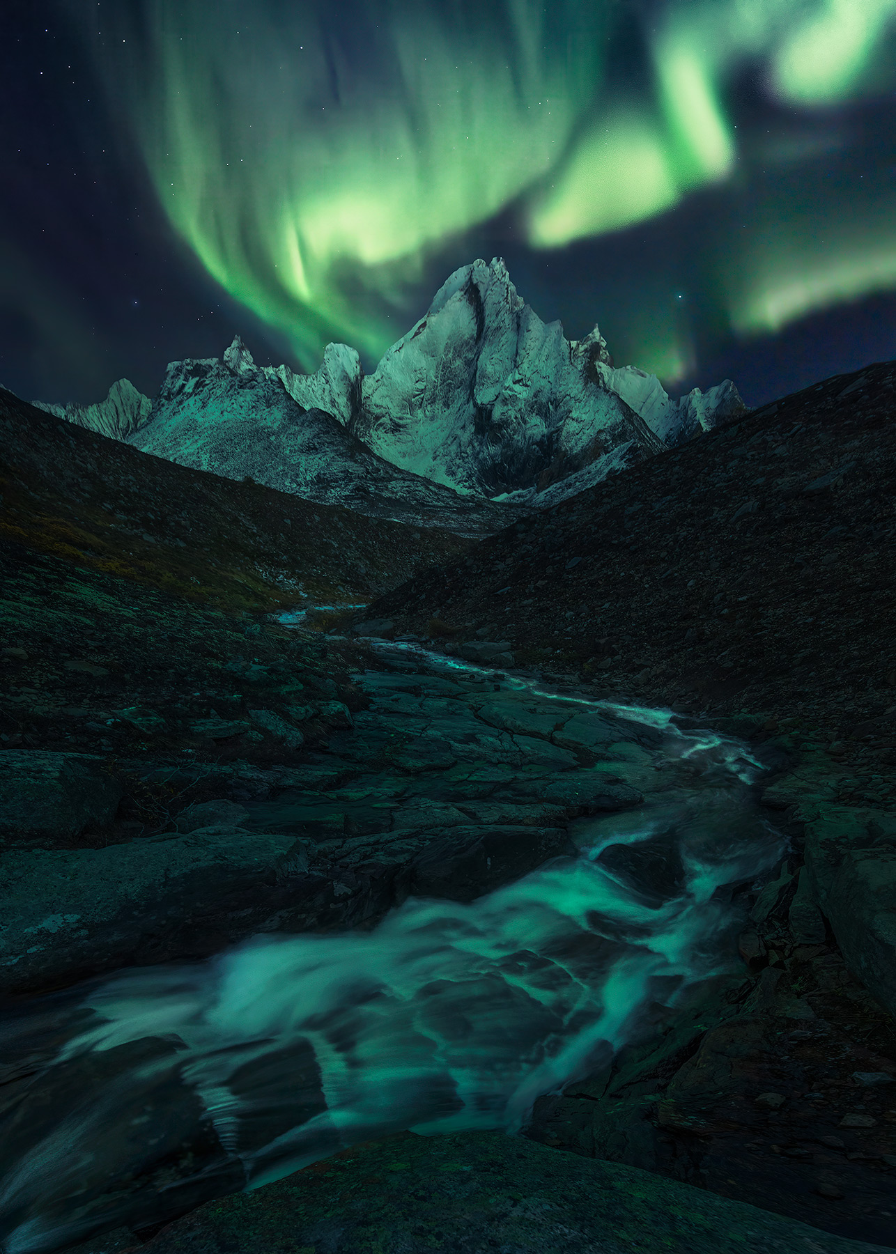 A long and winding stream makes it's way to the Monolith massif, in Canada's Yukon, under the light of the aurora.