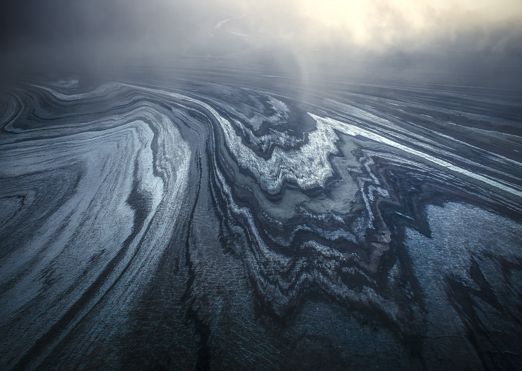 Into the Void Glacial ice patterns visible below the fog in Wrangell St Elias. The lateral moraines and ogives (striated lines...
