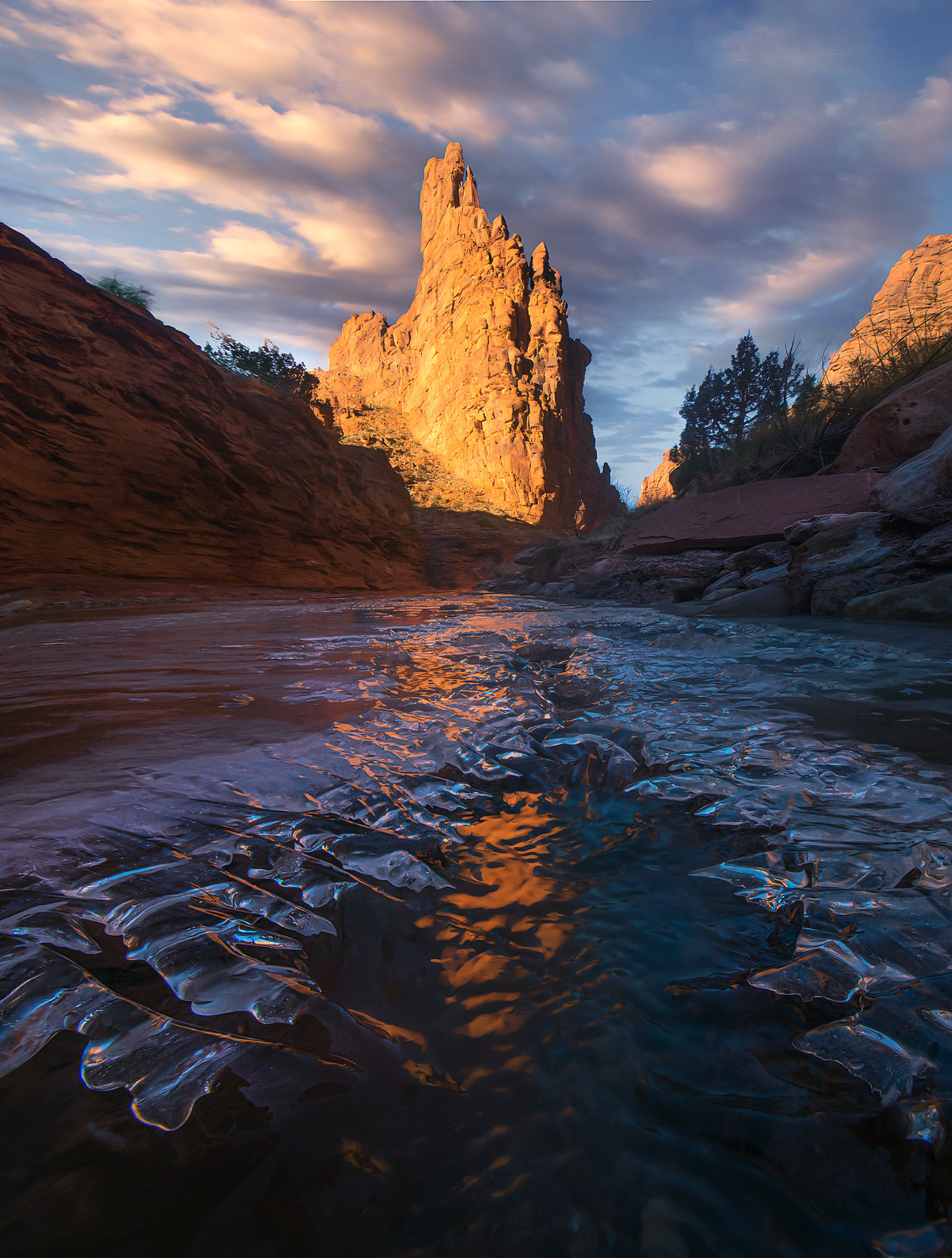 Red rock towers catch the sunrise light reflected in an icy stream