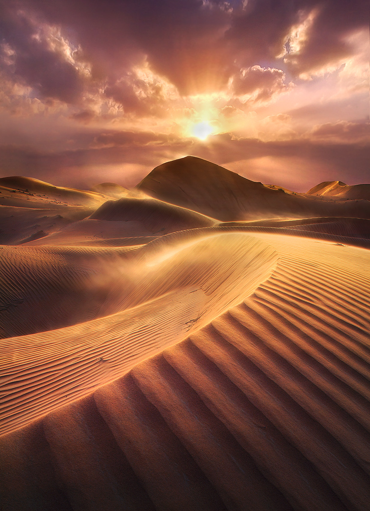 A windy sunset on the dunes looking towards light beams and vibrant skies. Taken near Dubai, United Arab Emirates.