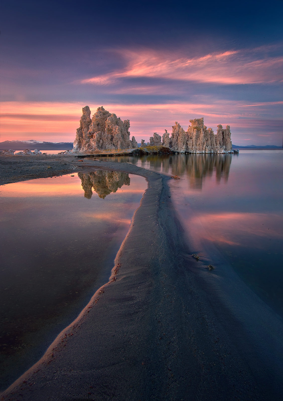 A long sandbar leads the eye towards dramatic Tufa formations as sunset clouds catch the light at Mono Lake, California.