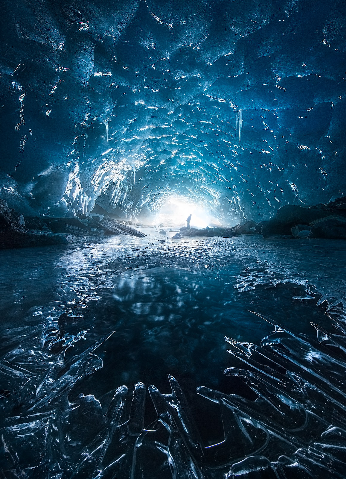 A lone figure stands under an icy cave in early winter in one of the middle of one of the most remote mountain ranges in the...