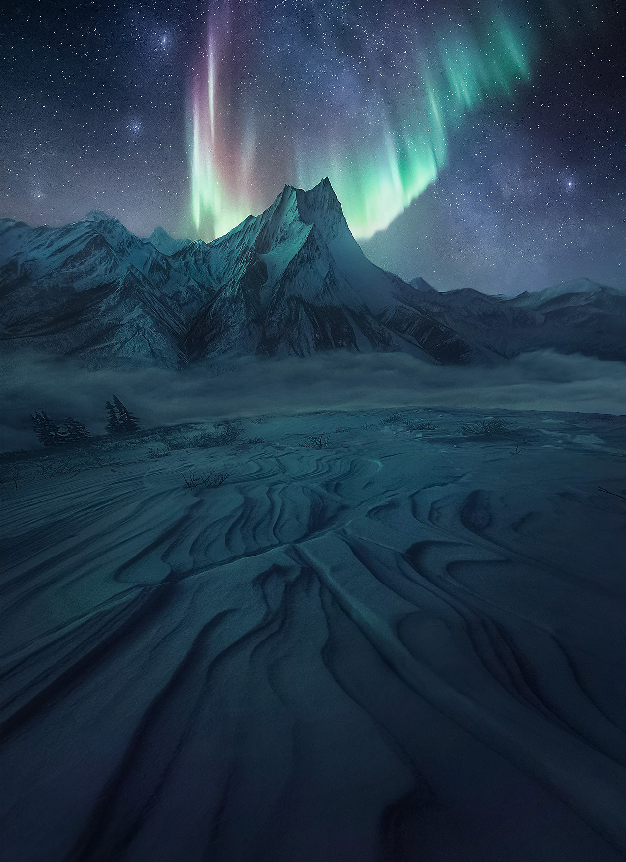 High peaks of Arctic Alaska depicted in faint moonlight below the aurora and Northern band of the Milky Way