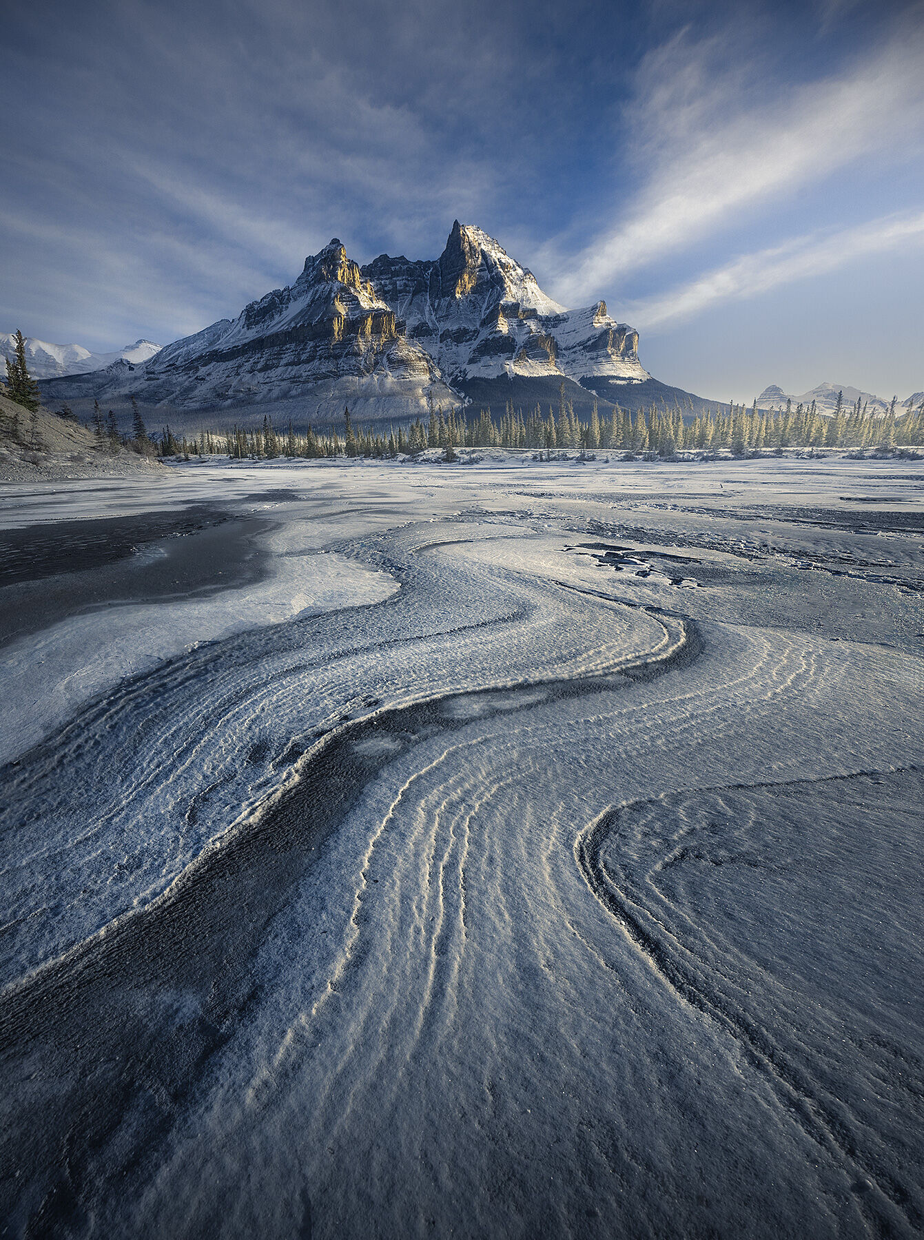Wind blown snow formations called sastrugi lead to the peaks and light along Saskatchewan River.