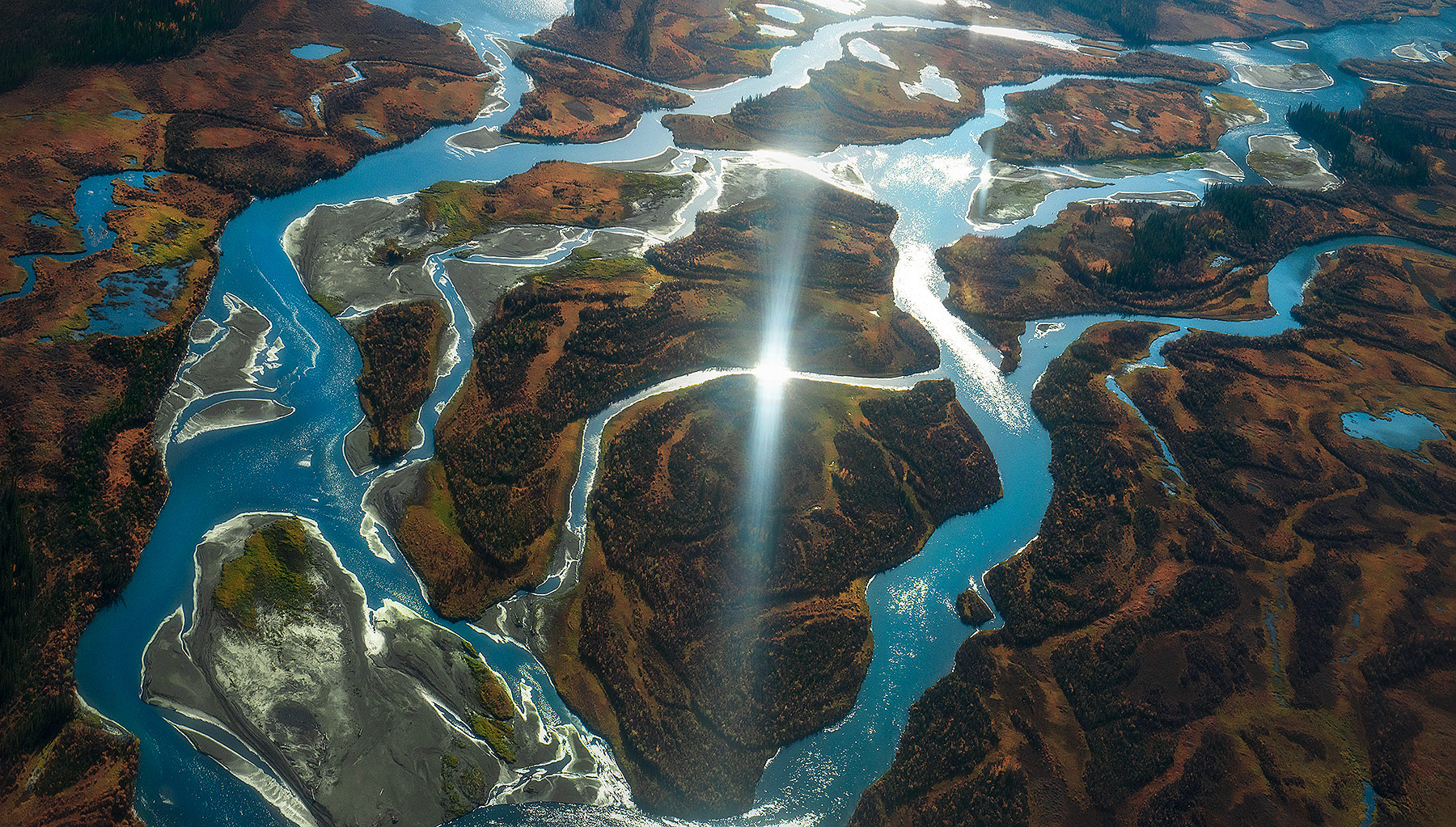 The sun reflects in glacial blue rivers crisscrossing autumn colors which adorn Canada's Far North