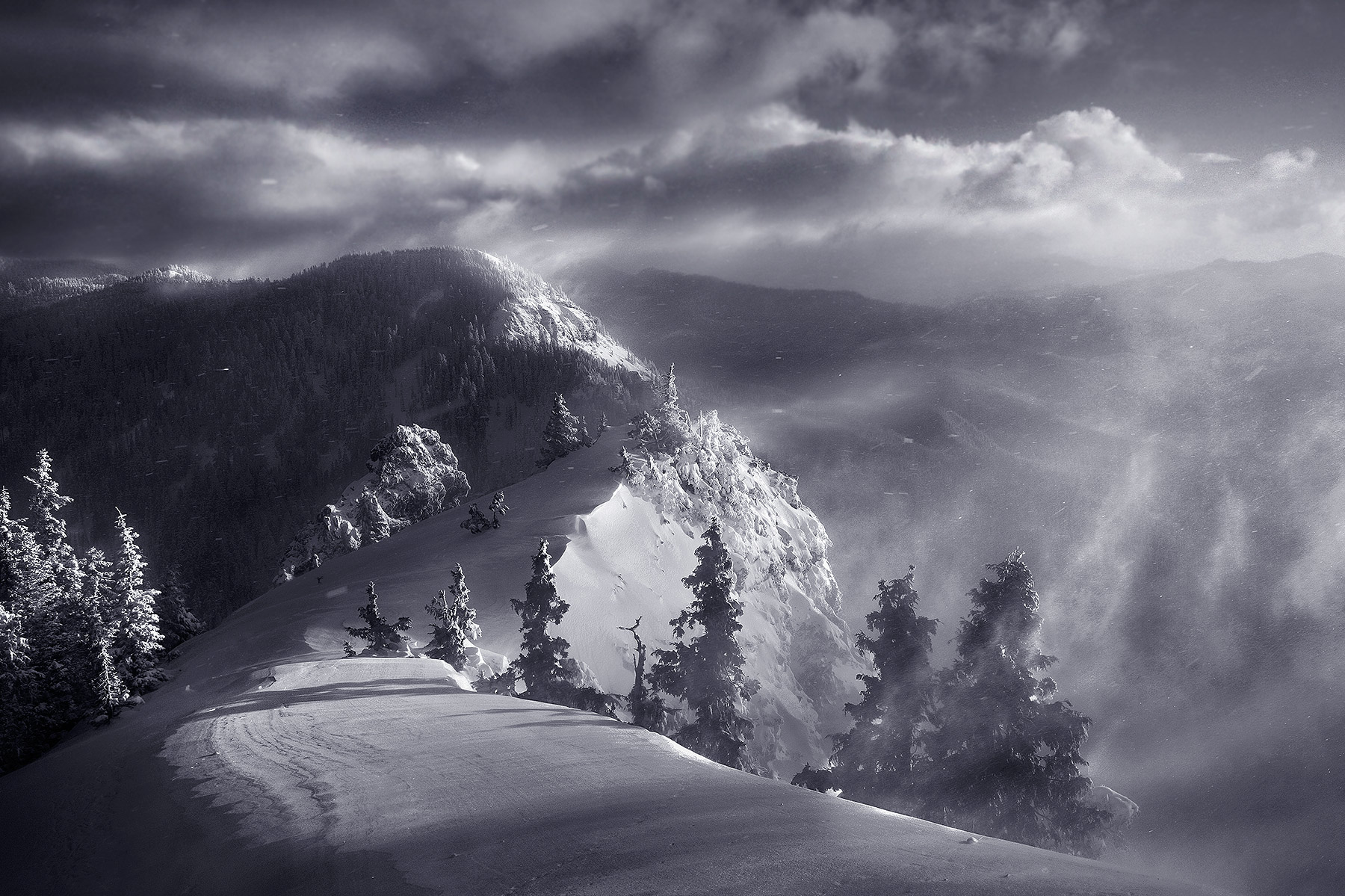 Furious conditions atop a peak in Oregon's Cascade range in the middle of Winter. Blowing snow streaks across the landscape.