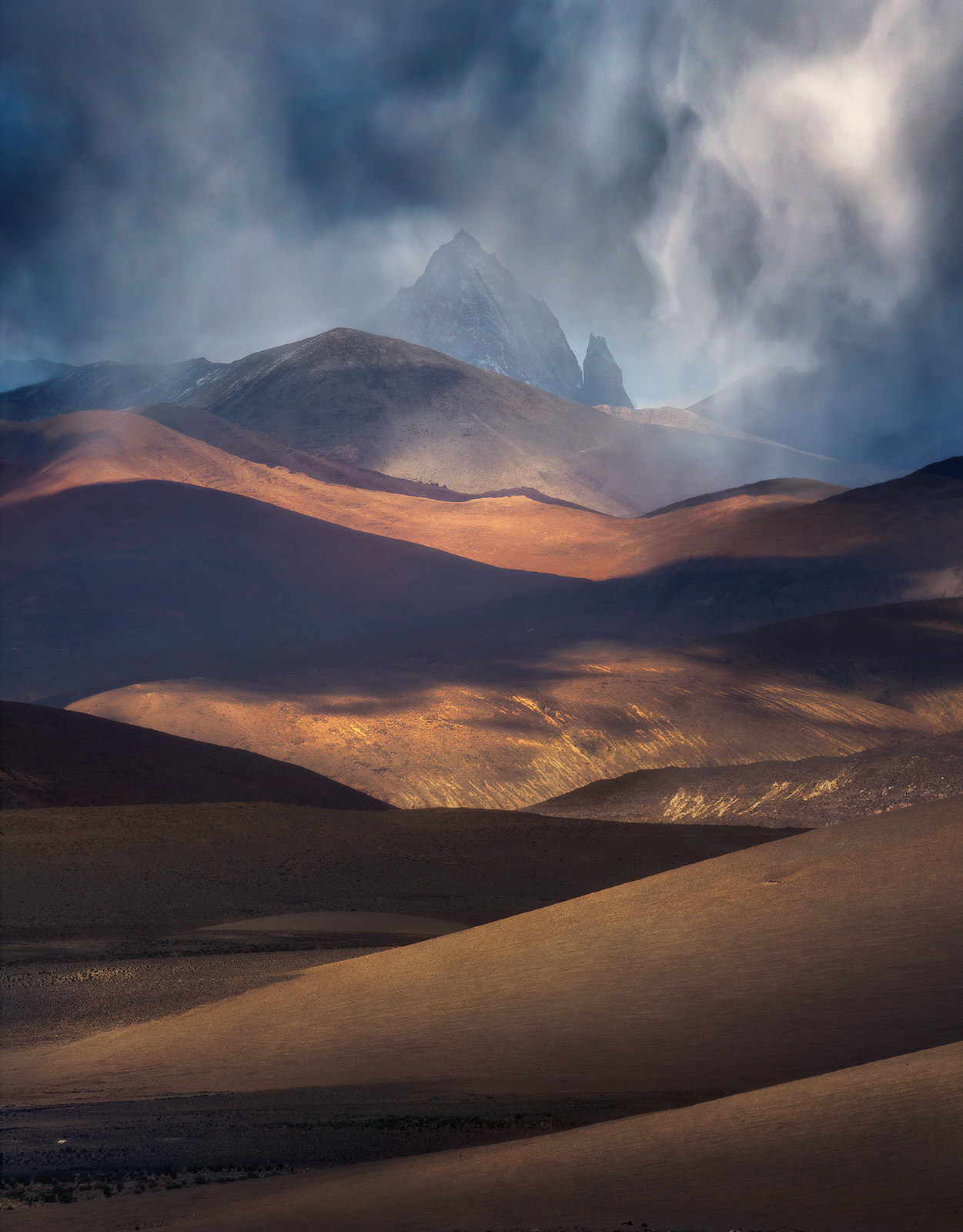 The rugged layered landscape of Tibet darkens beneath an approaching summer storm.&nbsp;